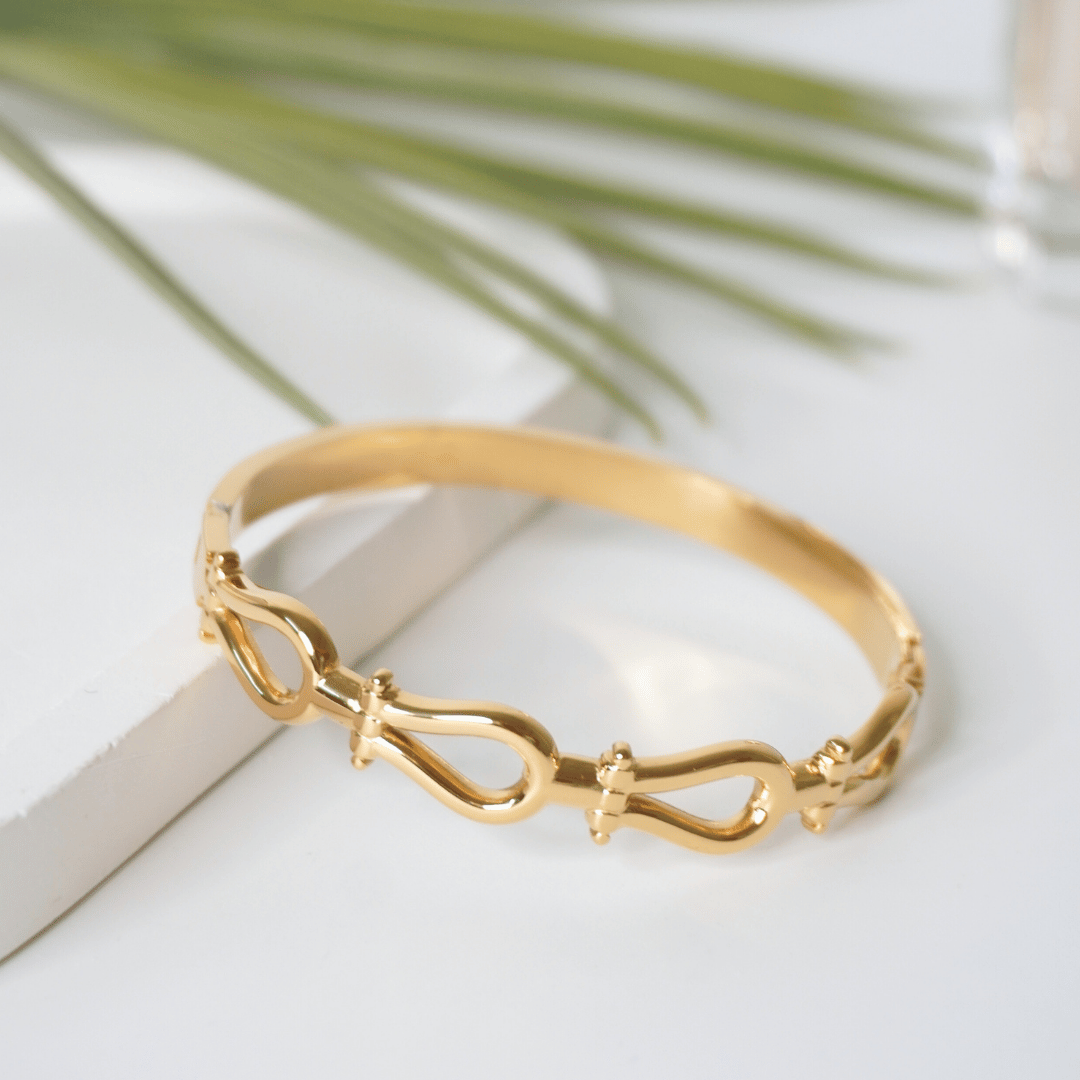 Gold bracelet on a white surface with a leafy background